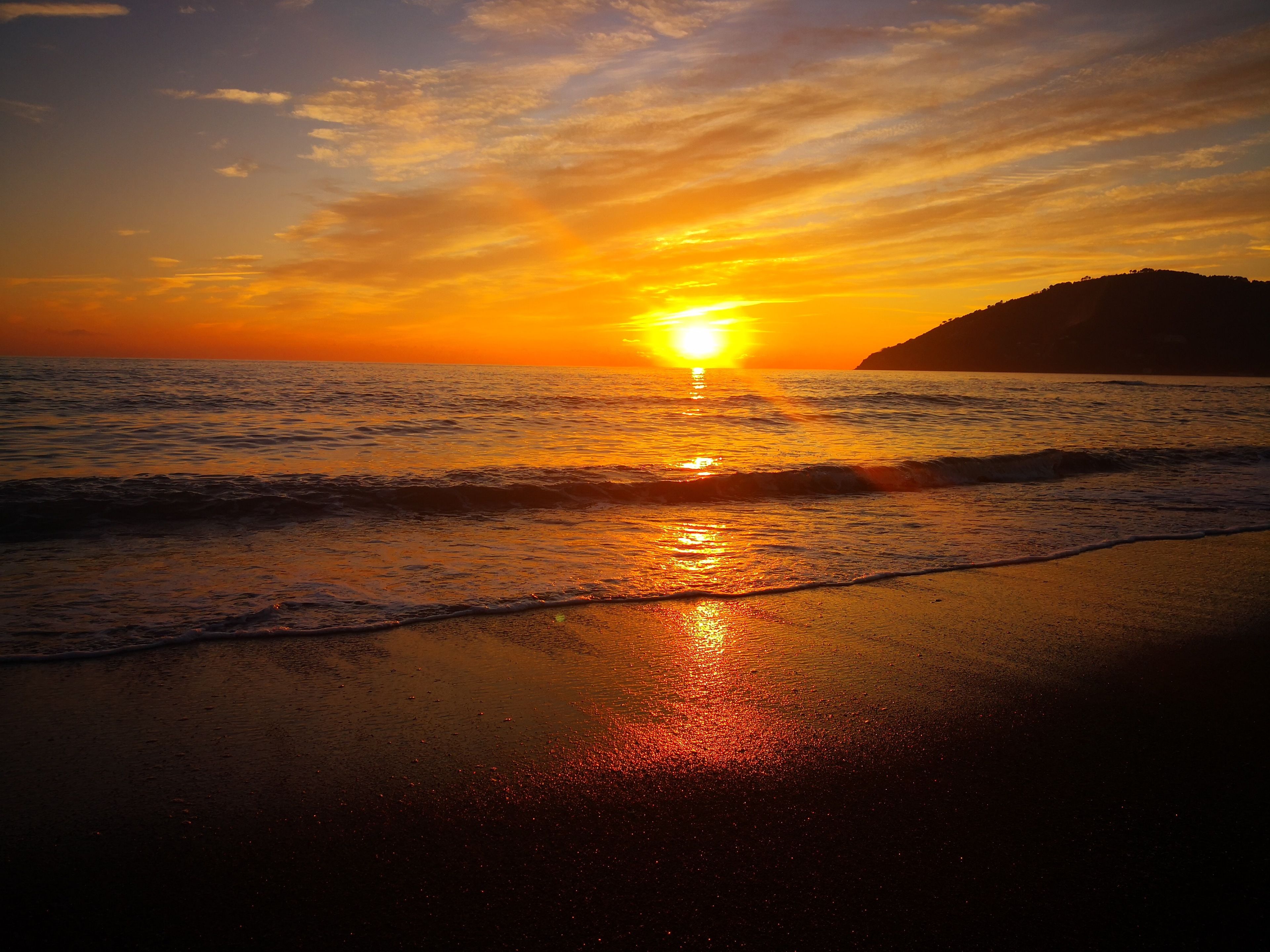 A sunset over the ocean with waves on the shore.