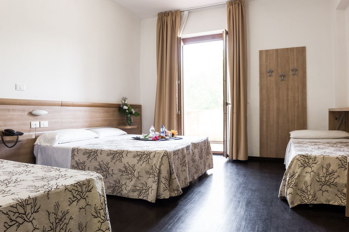 A hotel room with two beds, a wooden headboard, a small table with a floral arrangement, and a wooden wardrobe.