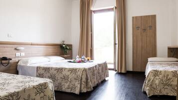 A hotel room with two beds, a wooden headboard, a small table with a floral arrangement, and a wooden wardrobe.