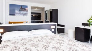 Habitación de hotel moderna con una cama grande, un escritorio integrado, un espejo y una imagen de un edificio costero.