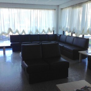 A living room with a sectional sofa, a coffee table, and a view through sheer curtains. - Hotel Rondine (Sarzana)