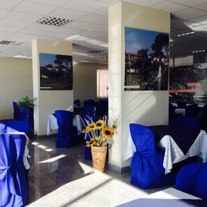 A restaurant with blue-covered chairs, a vase of sunflowers, and framed pictures on the walls. - Hotel Rondine (Sarzana)