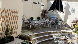 Un patio con sillas y mesas de metal, una parrilla y un muro decorativo con diseño de celosía.