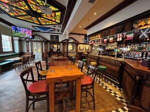 Una zona de bar con mesas y sillas de madera, una barra con diferentes botellas y un techo de vitrales.