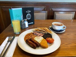 Een ontbijtbord met bonen, worstjes, eieren en toast, vergezeld van een glas sinaasappelsap en een kop koffie.