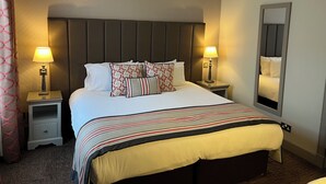 Una cama bien hecha con una colcha a rayas, dos mesitas de noche con lámparas, un cabecero y un espejo en la pared.