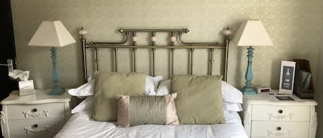 A neatly made bed with white linens and two pillows, flanked by two bedside tables with lamps and a small clock.
