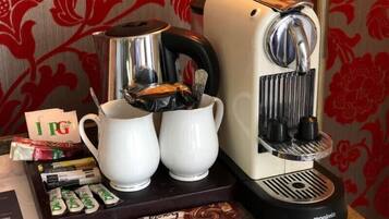 A coffee machine with two white cups, a tray with coffee pods, and a packet of Galantine chocolate.