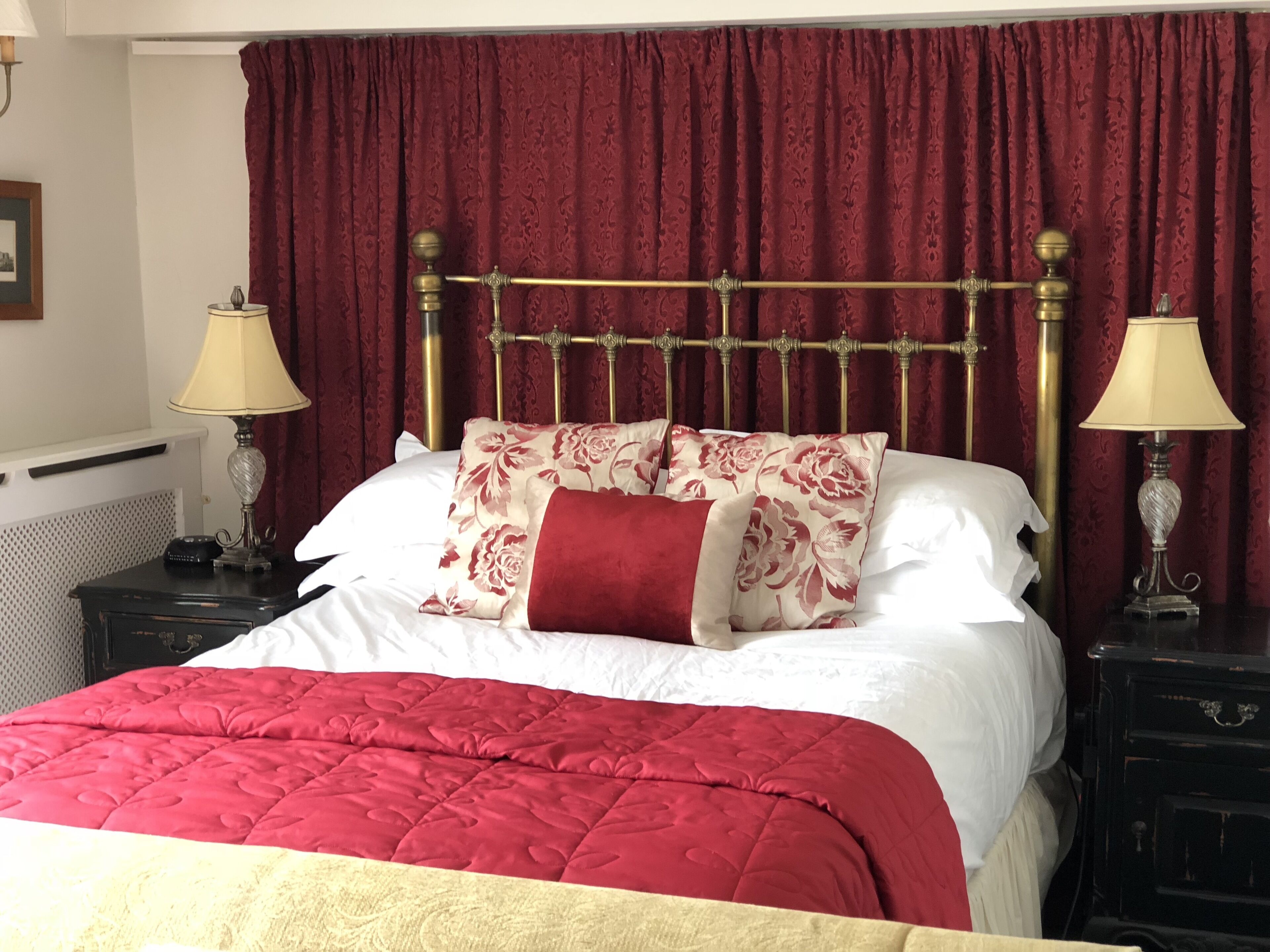 A bed with a red and white quilt, two bedside lamps, and a red curtain.
