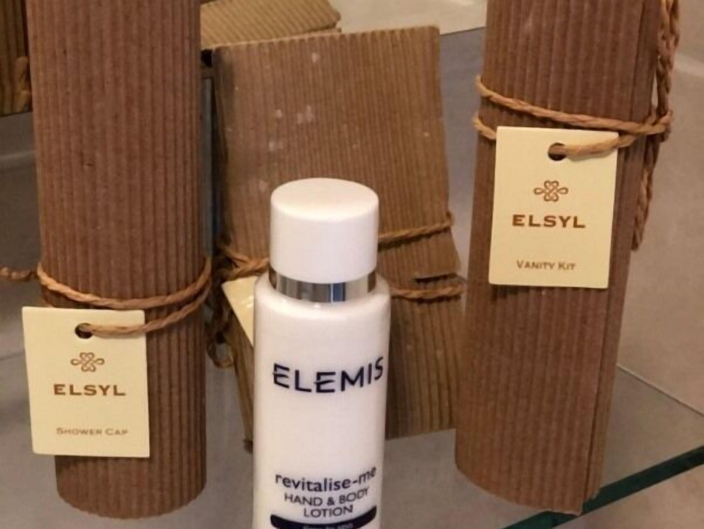 A bathroom with wooden pillars, a shower cap, and a bottle of Elemis hand and body lotion.