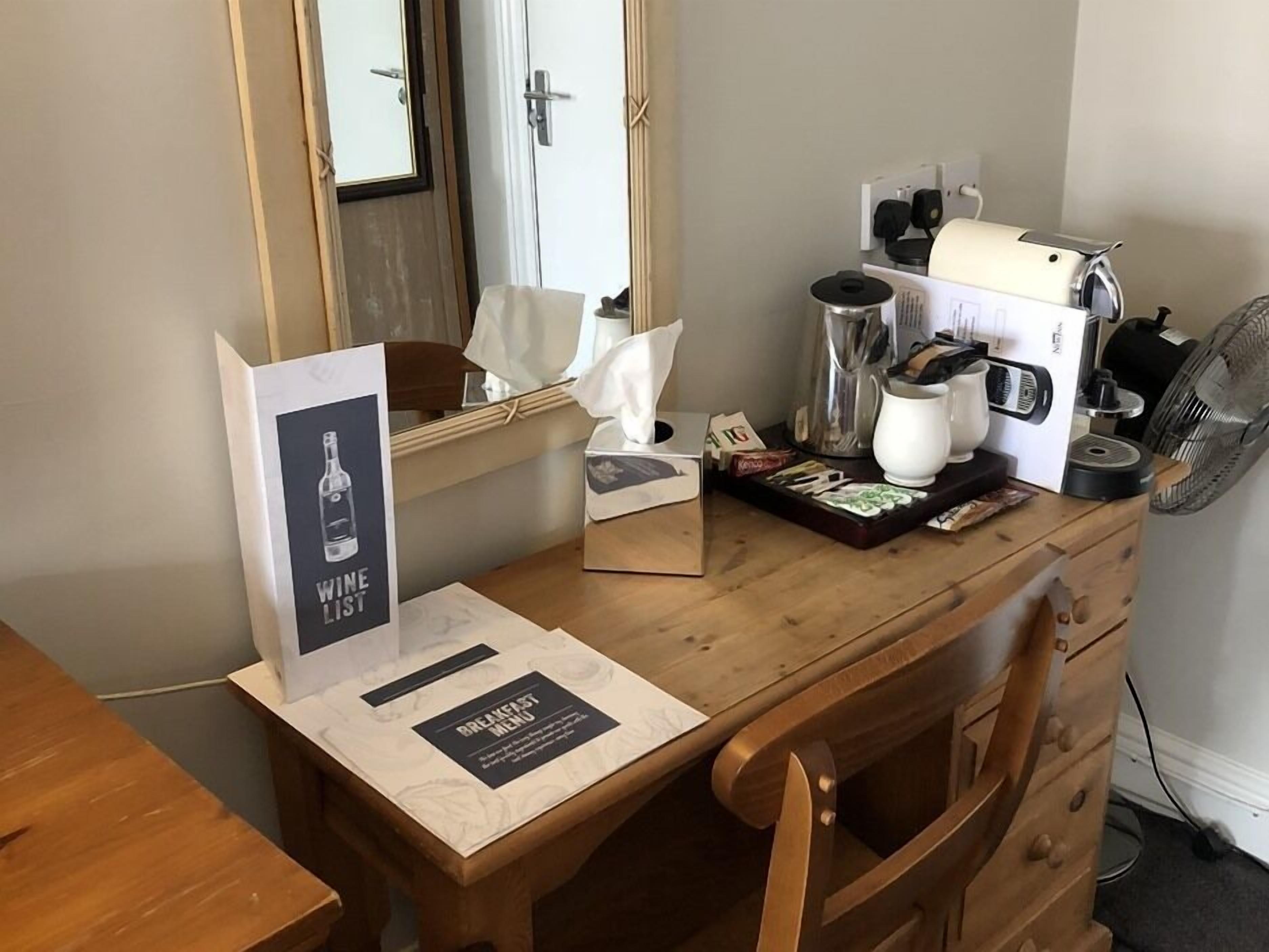 Un taulell de fusta amb un cartell del menú de vins, un menú d'esmorzars, una caixa de mocadors, una cafetera, un búl i un ventilador.