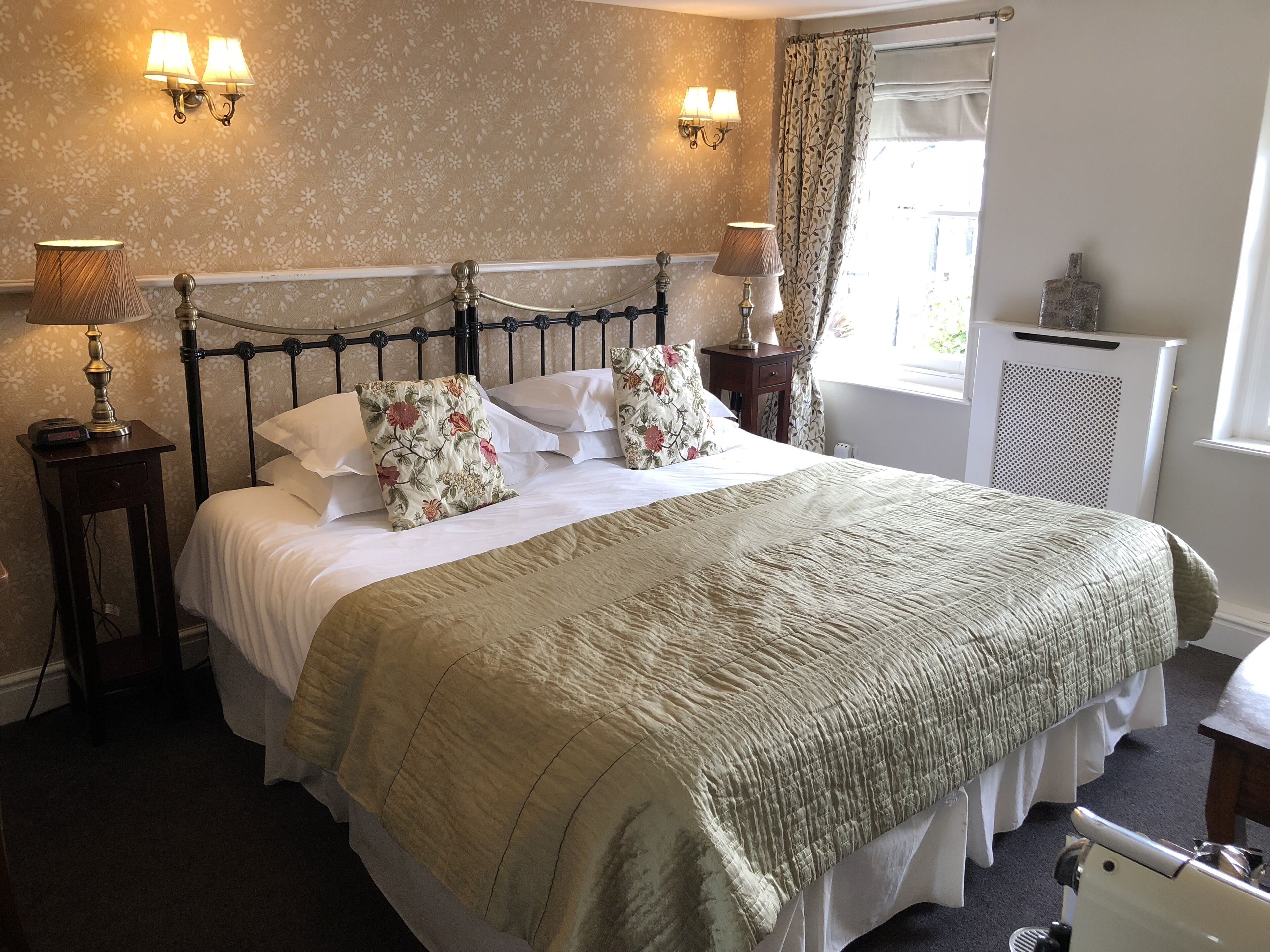 A neatly made bed with floral pillows, a bedside lamp, and a nightstand with a lamp.