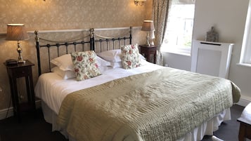 A neatly made bed with floral pillows, a bedside lamp, and a nightstand with a lamp.