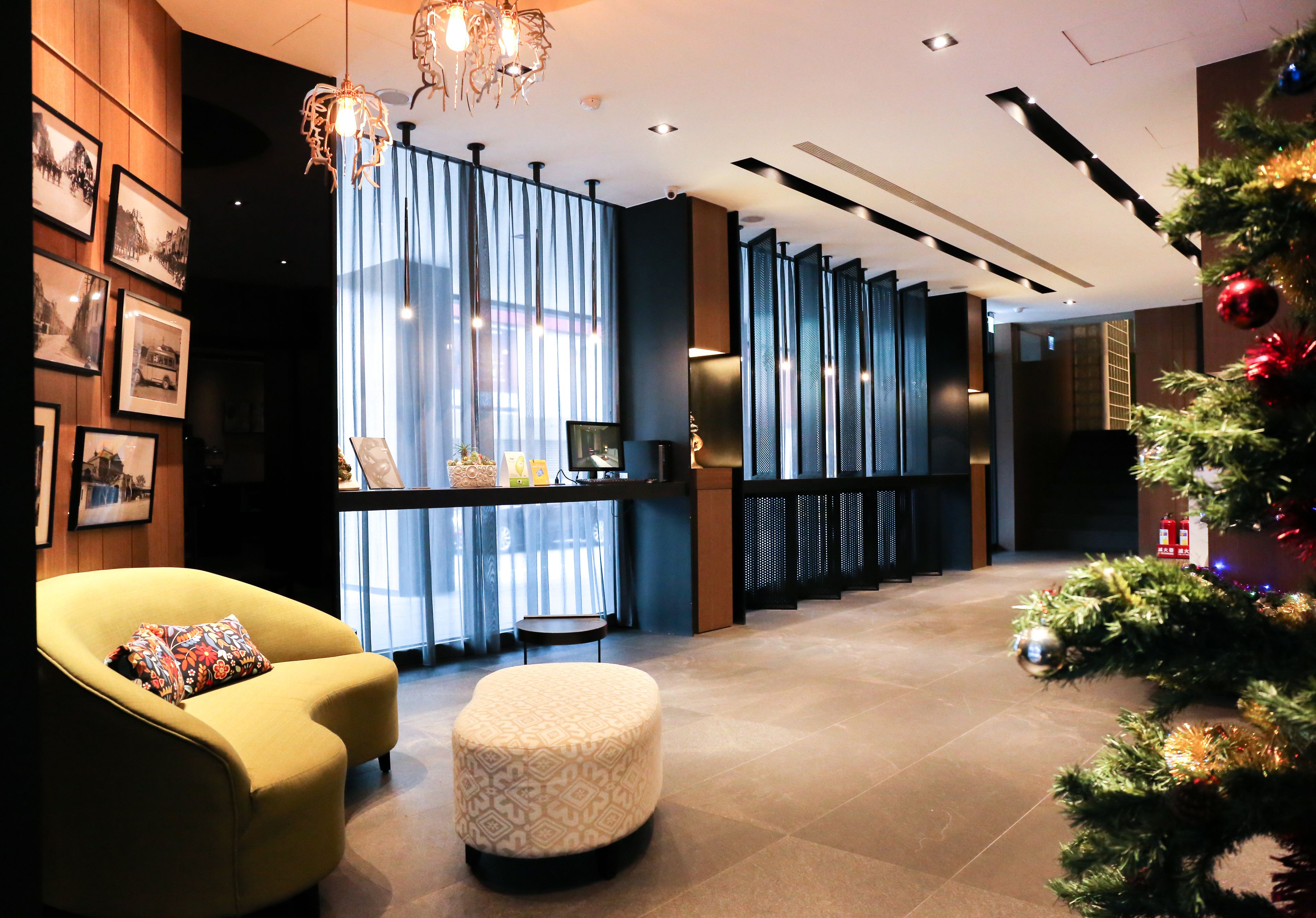 A modern lobby with a yellow armchair, a patterned ottoman, and a Christmas tree.