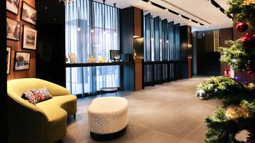 A modern lobby with a yellow armchair, a patterned ottoman, and a Christmas tree.