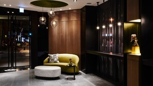 Un hall d’entrée moderne avec un canapé jaune, un pouf à motifs et des luminaires suspendus.