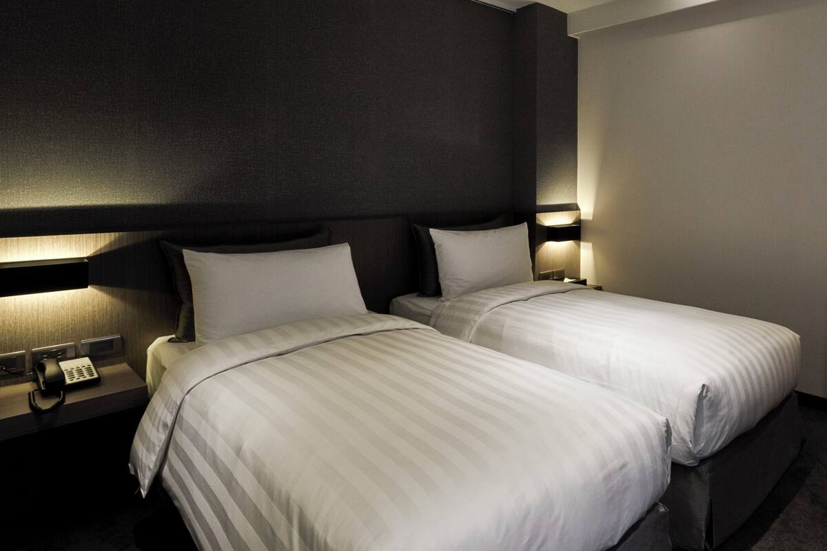 Une chambre d’hôtel avec deux lits, des murs sombres et des lampes de chevet.