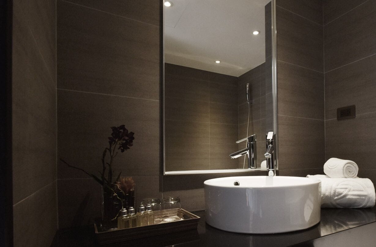 Un baño moderno con un espejo grande, un lavabo redondo y una cabina de ducha de vidrio.