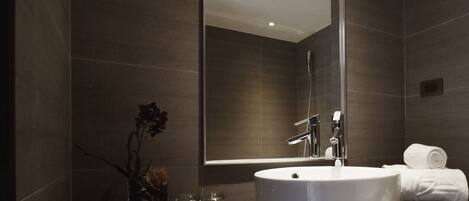 Un baño moderno con un espejo grande, un lavabo redondo y una cabina de ducha de vidrio.