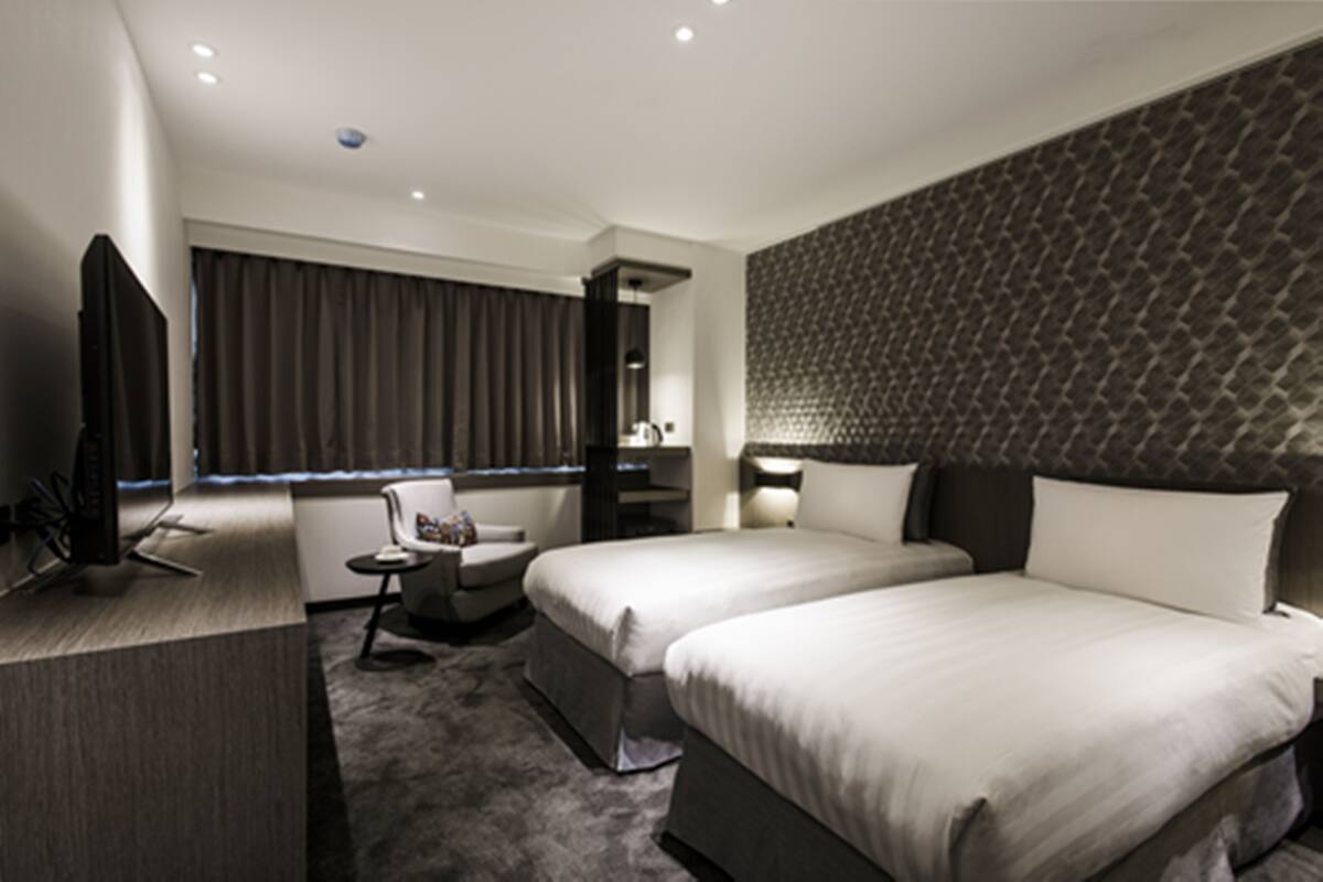 Une chambre d’hôtel moderne équipée de deux lits, d’un bureau, d’une chaise et d’un téléviseur.