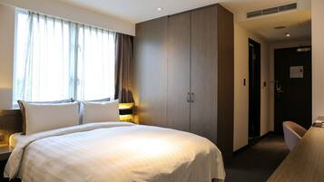 A hotel room with a large bed, a wardrobe, a desk, and a chair.