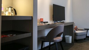 Une chambre d’hôtel moderne équipée d’un bureau, d’un téléviseur à écran plat, d’une chaise, d’une petite table et d’une poubelle.
