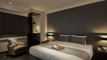 A modern hotel room with a large bed, a chair, bedside tables with lamps, and a window with curtains.
