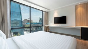 Ein Hotelzimmer mit einem großen Bett, einem Wand-Fernseher und Blick auf die Stadt durch große Fenster.