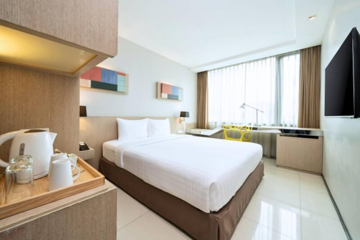 A modern hotel room with a large bed, a desk with a chair, a window with curtains, and a flat-screen TV.