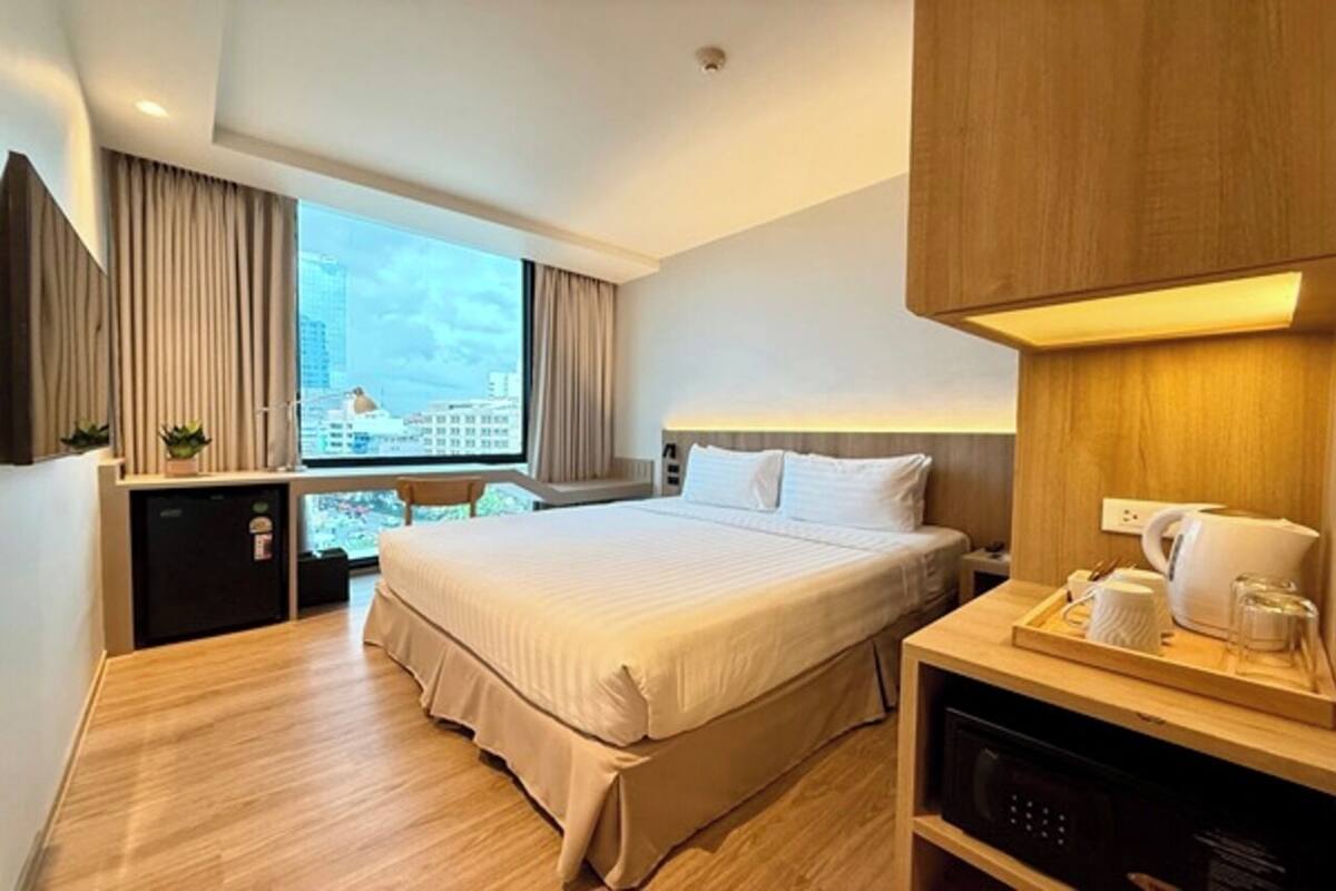A hotel room with a large bed, a desk with a coffee maker, a small fridge, and a view of the city.