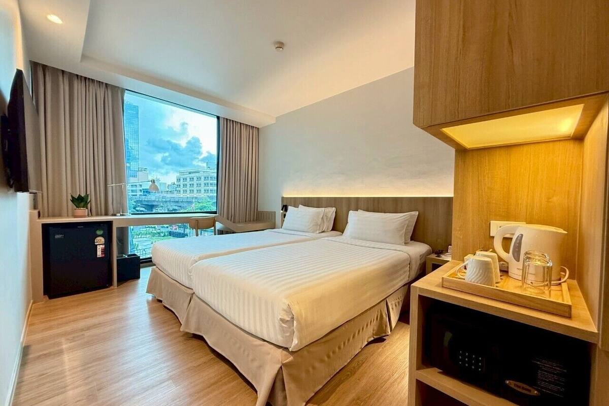 A modern hotel room with two beds, a small desk, a coffee maker, and a view of the city.