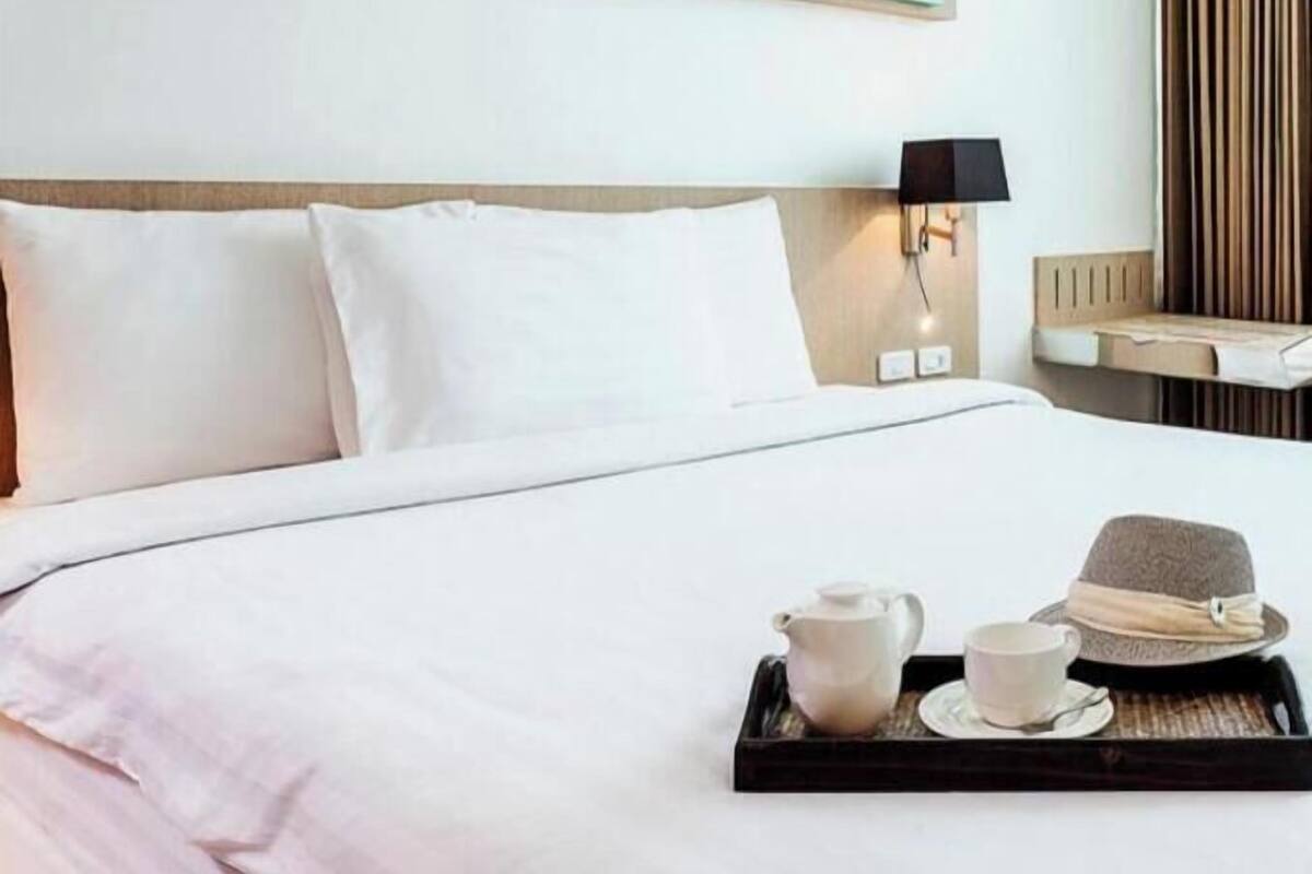 A hotel room with a bed, a tray with a teapot, cup, and hat, and two abstract paintings on the wall.