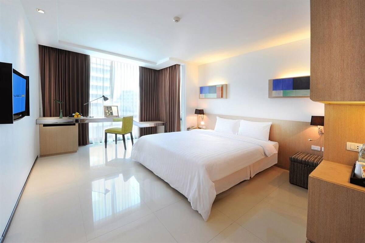 A hotel room with a bed, desk, chair, and a TV.