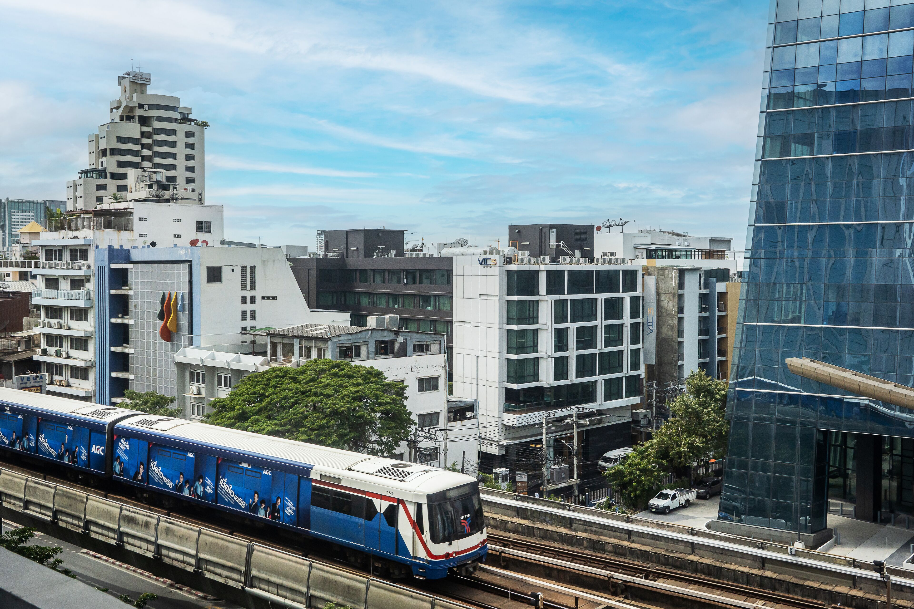 A modern train station with a blue and white train, surrounded by contemporary buildings and a clear sky.