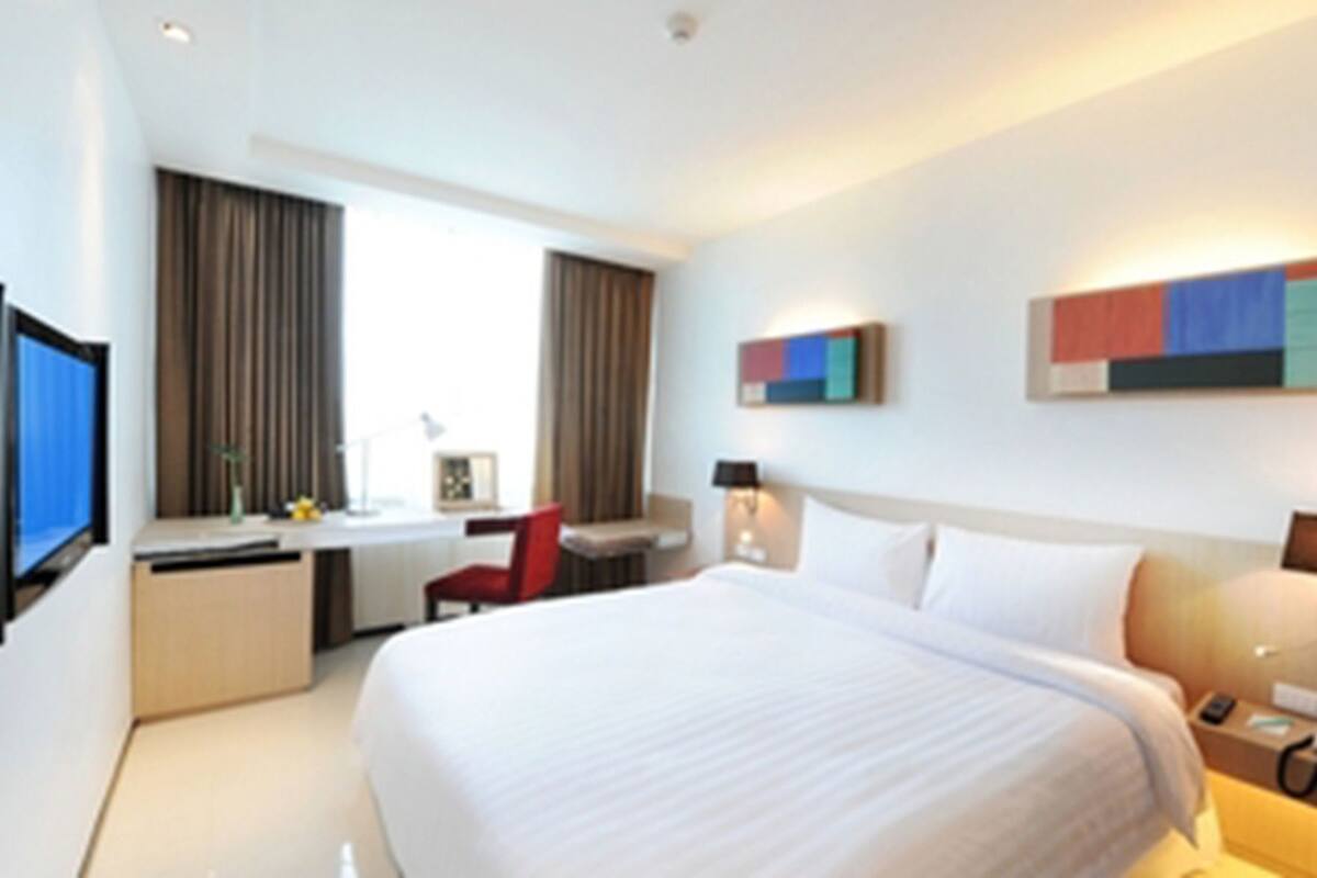 A hotel room with a bed, desk, chair, and a TV.