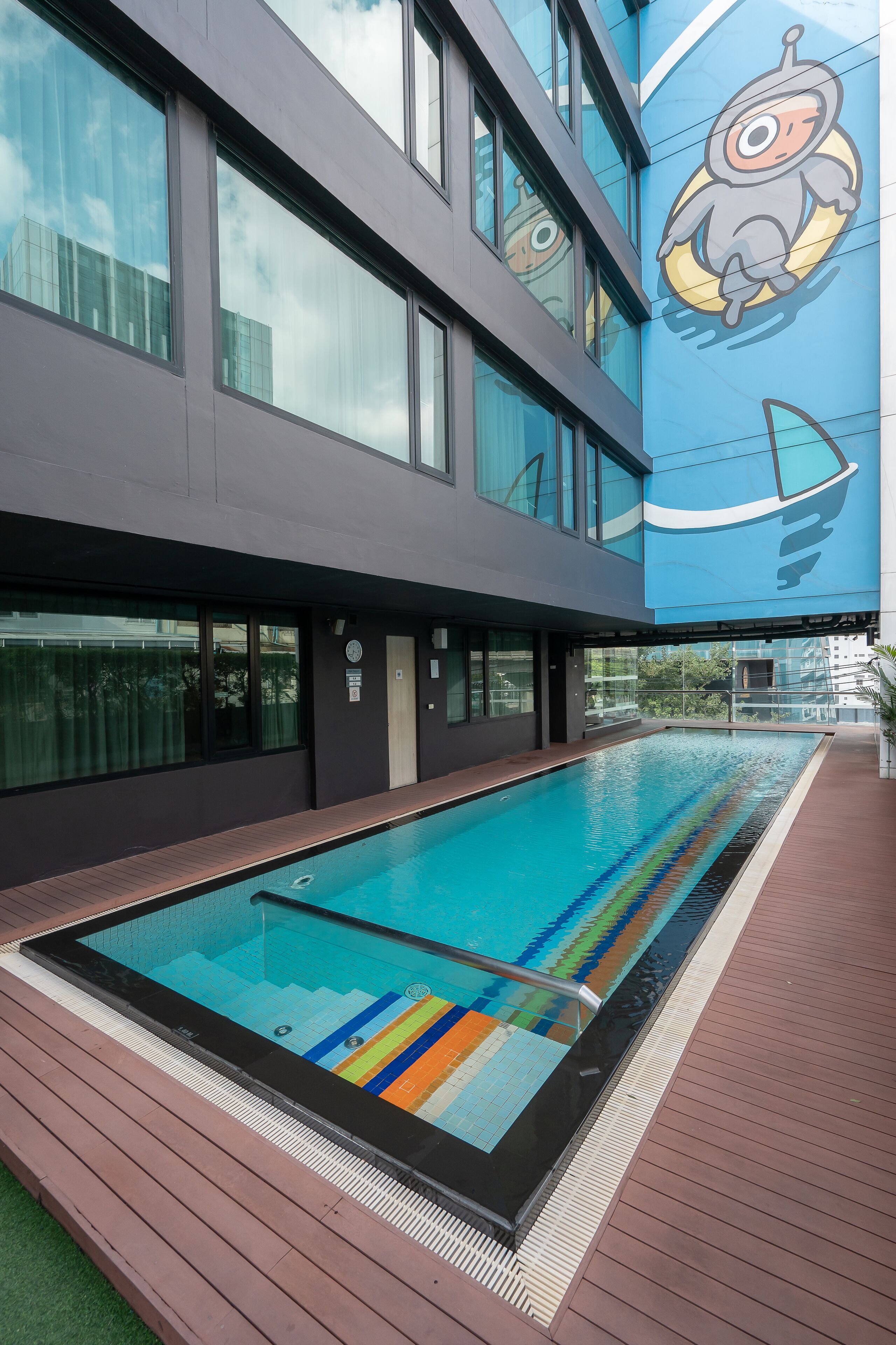 Un edificio moderno con piscina, ventanas amplias y un mural de un astronauta caricaturesco.