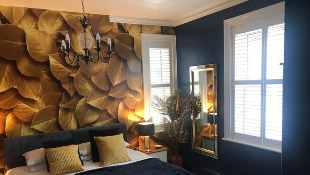 A bedroom with a large bed, a wall-mounted chandelier, and a mirror. - Amarillo (Bournemouth)