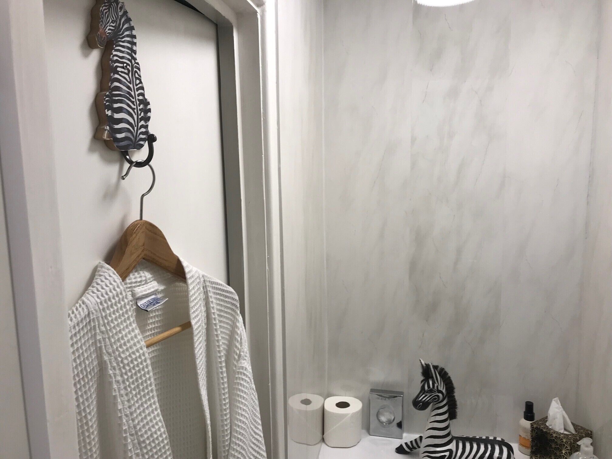 Un baño con una toalla de estampado de cebra colgada en un perchero de madera, un peluche de cebra en la encimera y una botella de desinfectante para manos.