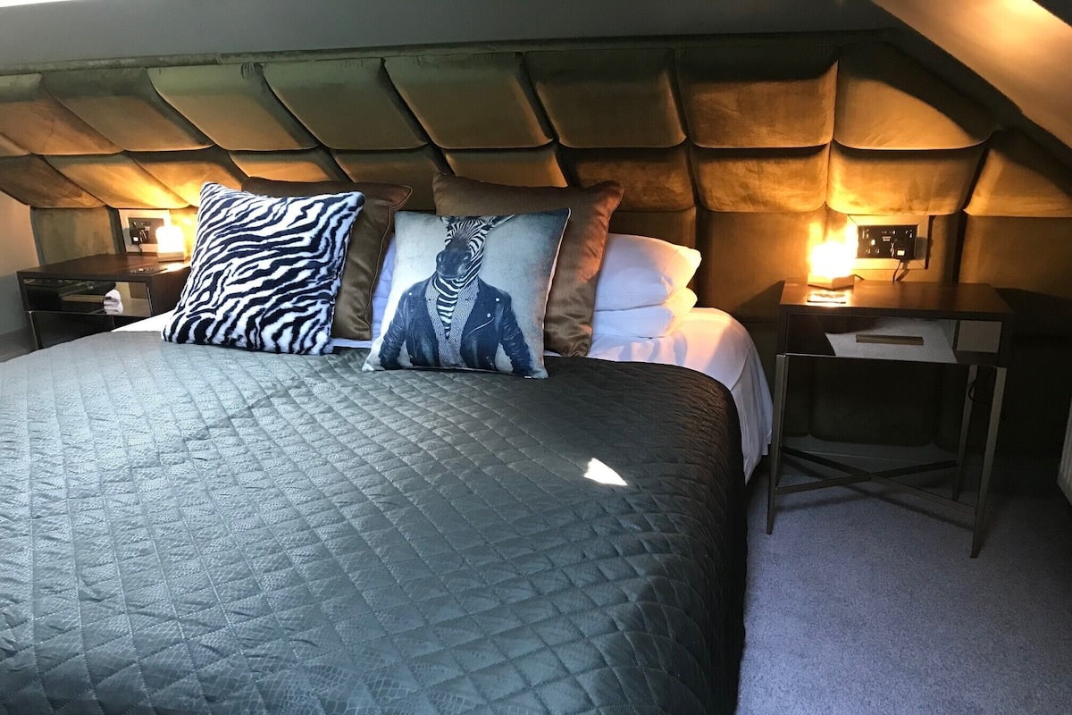 A bed with a quilted cover, two pillows with a zebra pattern, and a headboard with a tufted design.