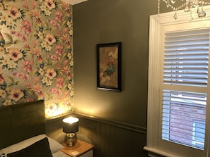 Cozy retreat with a floral wallpaper, framed artwork, and a comfortable bed featuring a wooden headboard and a bedside lamp.