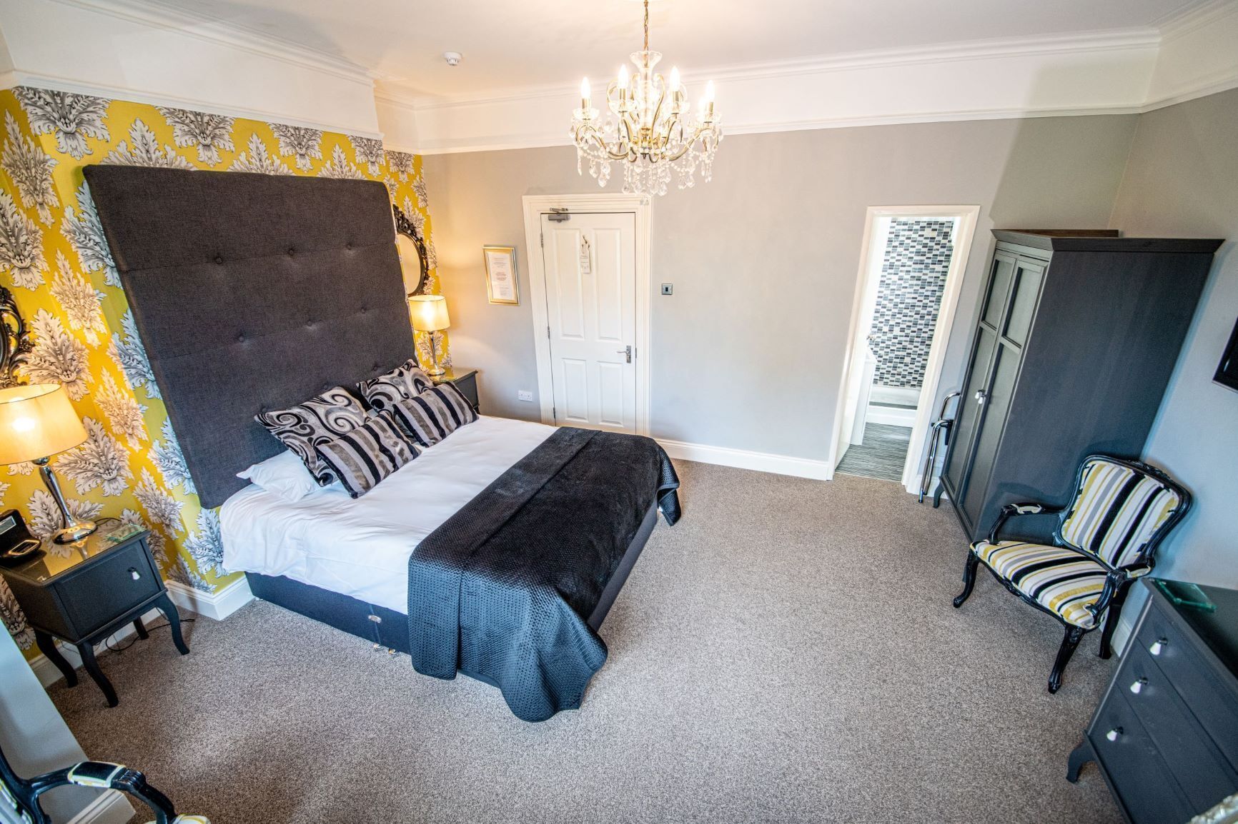 A bedroom with a large bed, a chandelier, a chair, and a wardrobe.