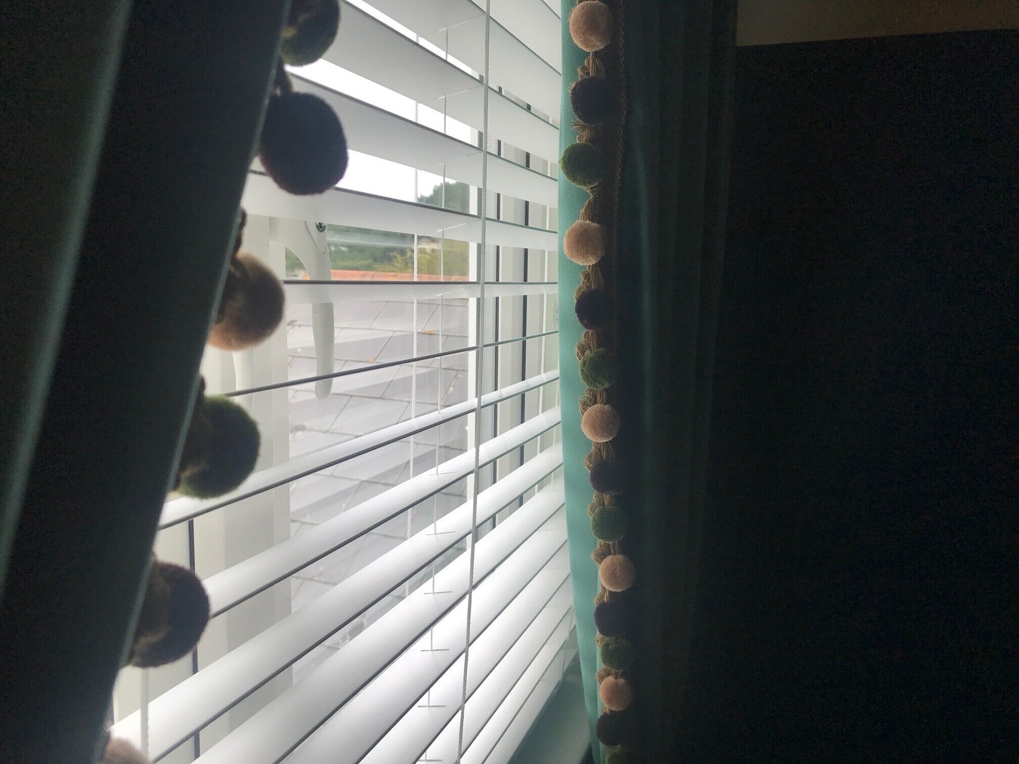A window with horizontal blinds and a curtain with pom-poms.