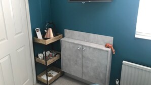 A small room with teal walls, a grey cabinet, a wooden shelf with items, and a mounted TV. - Amarillo (Bournemouth)