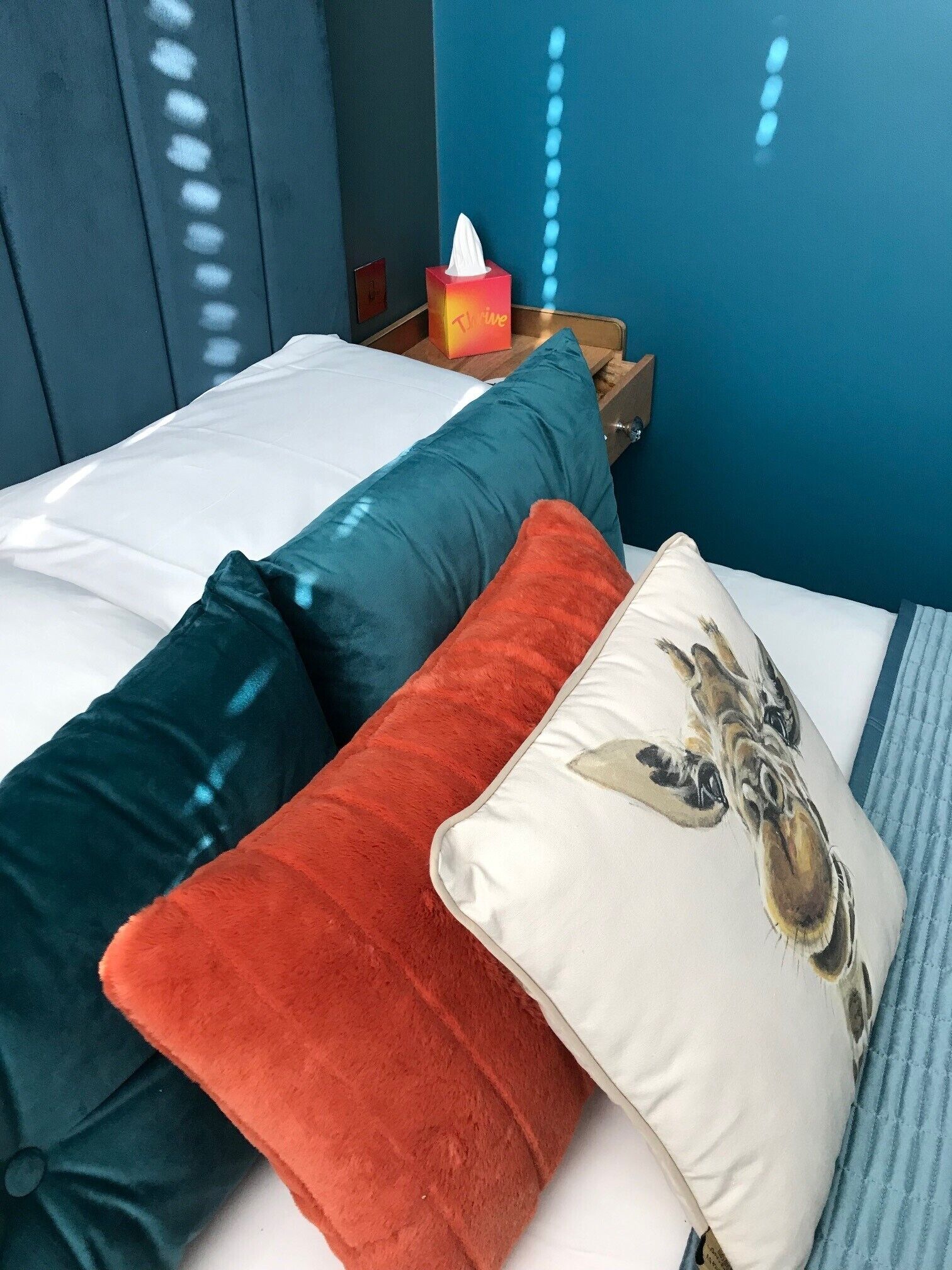 A bed with white bedding, teal and red pillows, and a white pillow with a giraffe design.