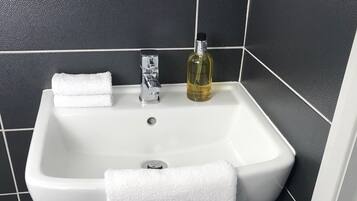 Une salle de bain avec un lavabo blanc, des carreaux noirs, un flacon de savon liquide et une serviette blanche posée sur un porte-serviettes en métal.