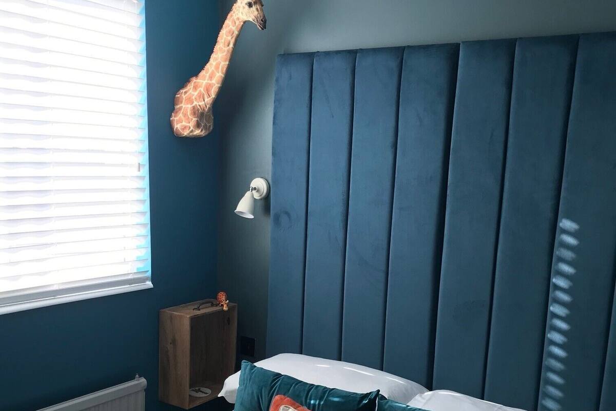 A bedroom with a blue headboard, a giraffe decoration, a nightstand, and a bed with multiple pillows.