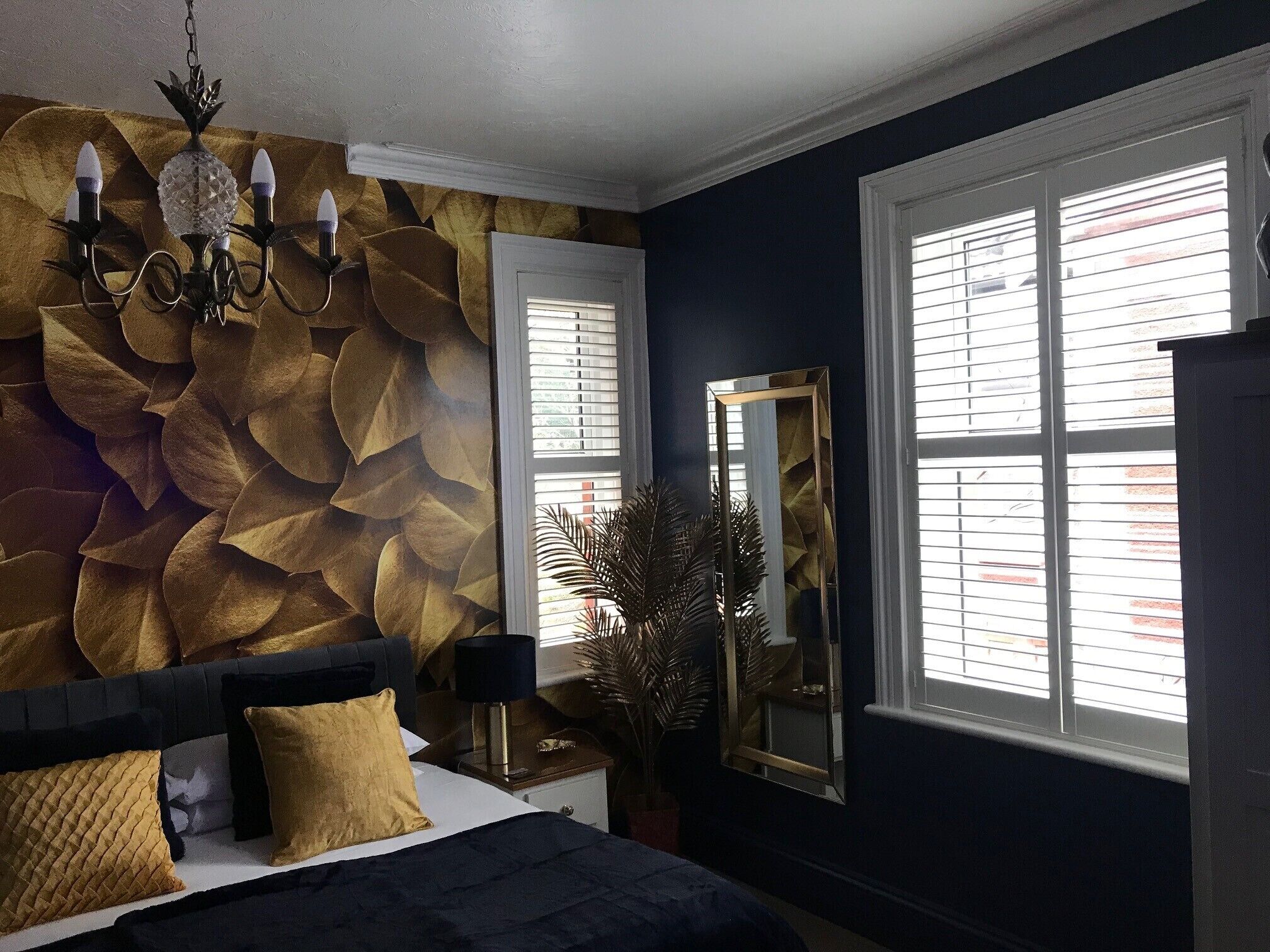 A bedroom with a large bed, a wall-mounted chandelier, a mirror, and a window with blinds.