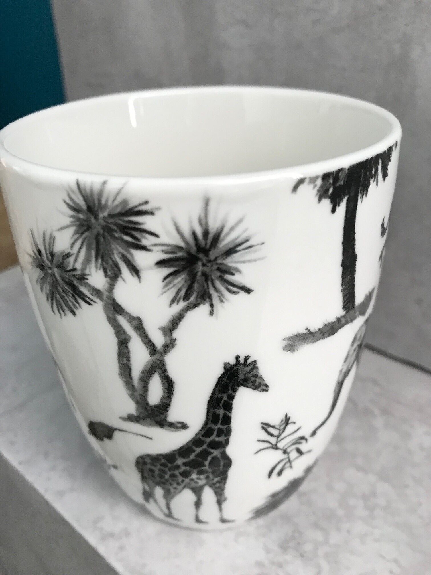 Una taza blanca con siluetas negras de una jirafa, palmeras y un árbol.