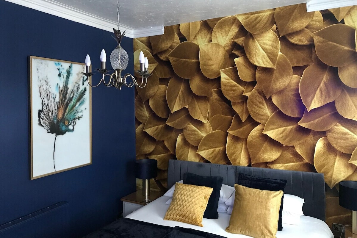 A bedroom with a large bed, a chandelier, a wall mural, and a framed artwork.
