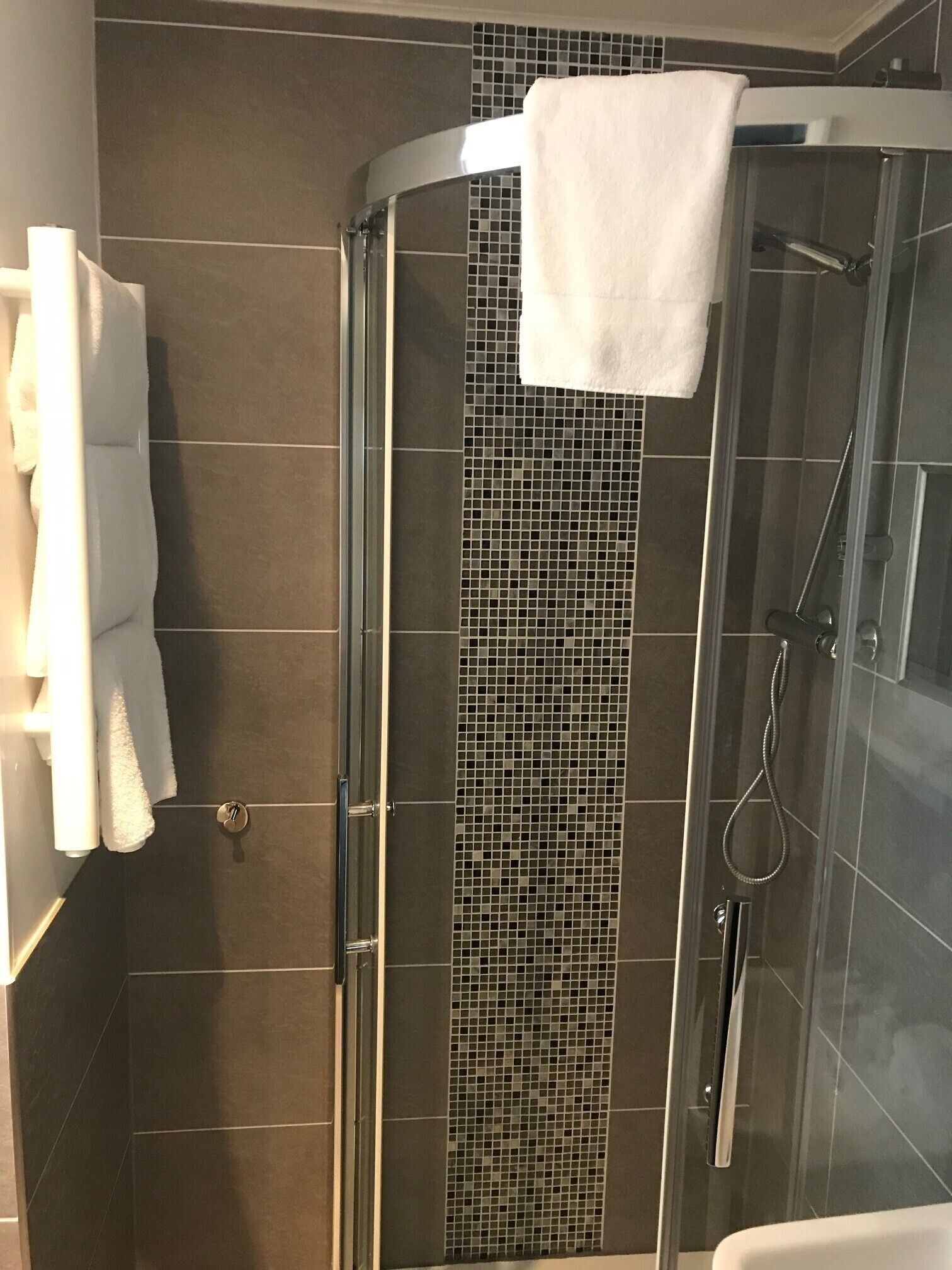 A glass-enclosed shower stall with a tiled wall and a white towel hanging on the door.